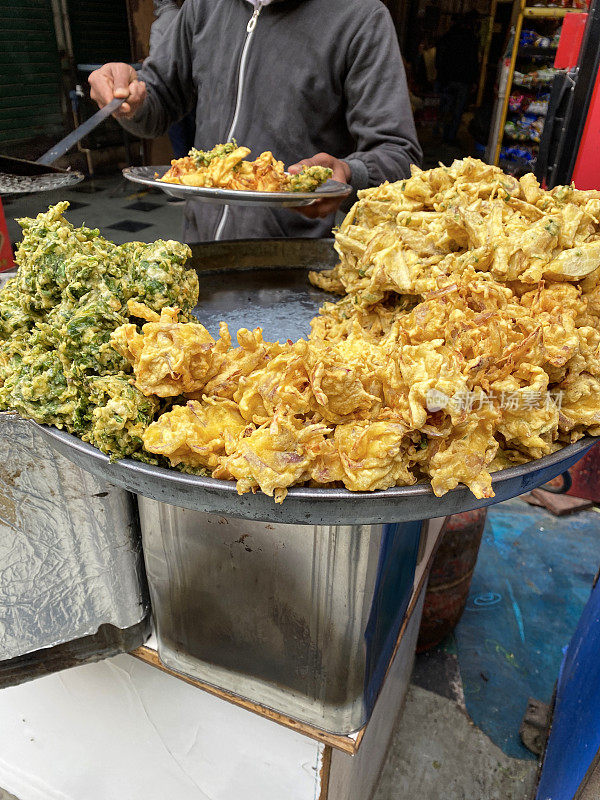 一堆酥脆的洋葱bhajis和palak pakora(菠菜馅饼)放在不锈钢的塔利(托盘)上，印度街头美食素食小吃，高架视野，重点放在前景